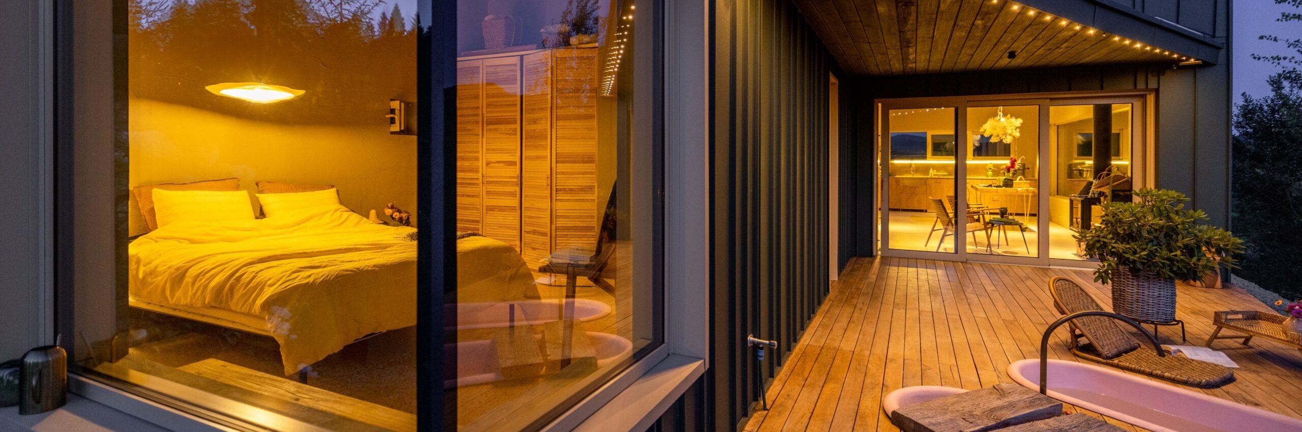 Evening glow from a cozy bedroom window with a pet dog looking outside. The wooden deck leads to an inviting interior illuminated by soft, ambient lights